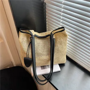 Dettaglio di borsa tote in paglia con manici neri in ecopelle su un davanzale