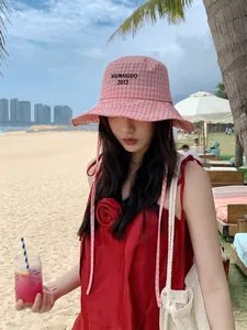 Donna asiatica che indossa un cappello a secchiello a scacchi rosa su una spiaggia soleggiata