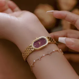 Nahaufnahme einer eleganten Uhr mit weinrotem Zifferblatt und goldenem Stahlarmband