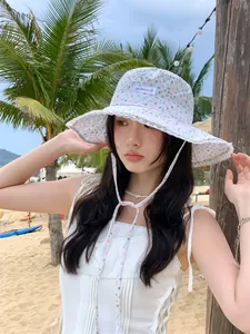 Close-up detail of a floral lace bucket hat with a wide brim worn by a model on a sunny beach