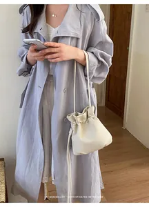 Chic cream drawstring bucket bag shown as a lifestyle accessory with a long trench coat