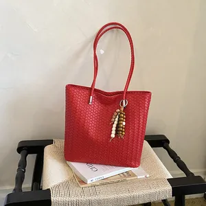 Μεγάλη κόκκινη πλεκτή δερμάτινη τσάντα με πολύχρωμο γούρι από χάντρες σε καρέκλα.