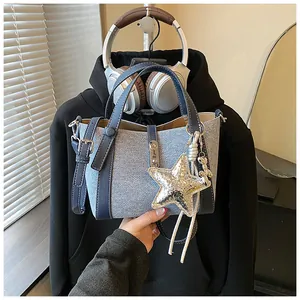 Detail view of denim texture bucket bag featuring a large metallic star charm and bear pendant