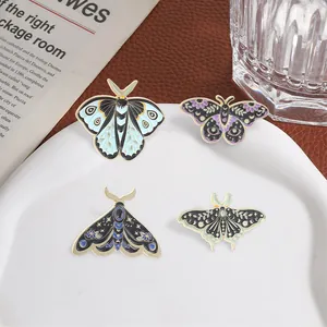Vintage moth and butterfly enamel pins with celestial and floral patterns on a plate