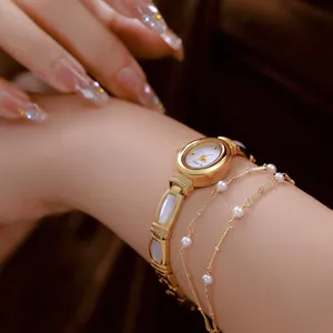 Primer plano de reloj de pulsera dorado con incrustaciones de nácar y cadenas de perlas