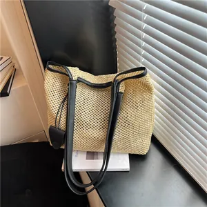 Vista dettagliata di una grande borsa tote in paglia con tracolle nere su un tavolo.