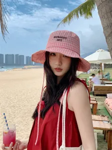 Primo piano di un cappello da pescatore a scacchi rosa con ricamo su una spiaggia soleggiata