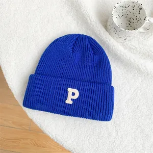 Close-up of blue knitted beanie with white embroidered letter P on textured background