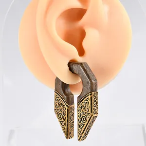 Détail rapproché de poids d'oreille en bois sculpté en U avec métal doré ornementé