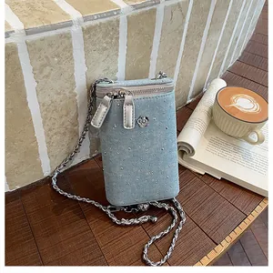 Close-up detail of a stylish denim crossbody phone bag with chain and camellia motif