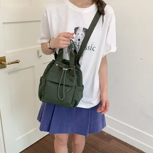 Mochila de nailon verde oscuro con cordón llevada por modelo en un estilo minimalista.