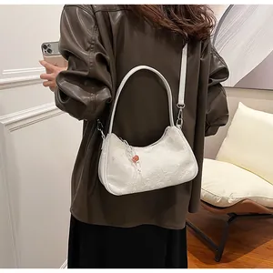 Detail view of a white textured underarm dumpling bag worn with a brown leather jacket.
