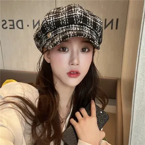 Detailed view of a black and white plaid newsboy hat with a gold heart pin on a model.