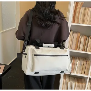 Large beige travel duffle bag carried by a person in a minimalist library scene.