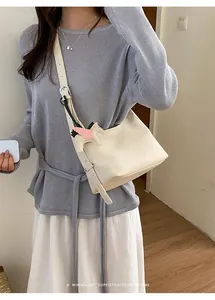 Elegant female model wearing a cream minimalist underarm shoulder bag with a charm