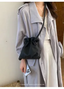 Detail view of a minimalist black drawstring bucket bag worn with a grey trench coat.
