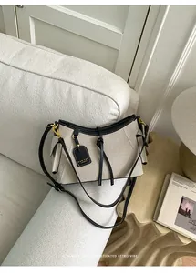 Vista detallada del bolso de lona beige con ribete de cuero negro sobre un sofá blanco
