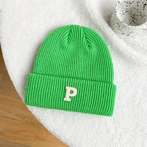 Detailed shot of a green knitted beanie with white P embroidery on a soft white rug.