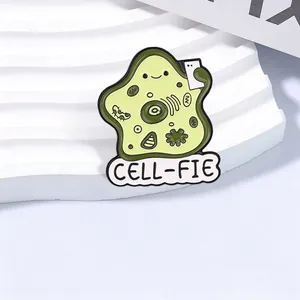 Close-up of a cute green cell selfie enamel pin with CELL-FIE text on a white stand
