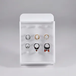White acrylic jewelry display board with lid showing various metal nose and septum rings