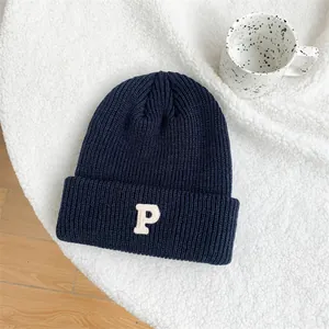 Macro view of a navy blue knitted beanie featuring a white embroidered letter P