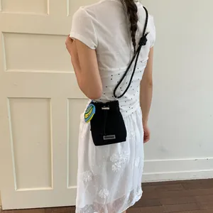 Detailed shot of a stylish black crossbody bucket bag with a rope strap and banana charm.