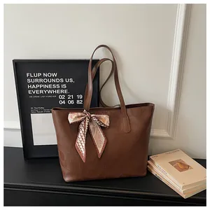 Detail of a large brown tote bag with geometric embossing and a decorative silk scarf