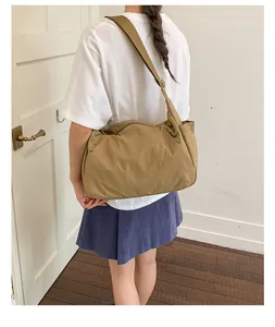 Detail view of a large khaki crossbody tote bag worn by a model in a minimal setting.