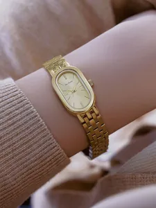 Primer plano de un elegante reloj ovalado dorado con correa de metal en la muñeca.