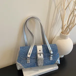 Blue denim baguette shoulder bag with silver studs and metallic buckles on white book.