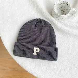 Detail view of dark grey knitted beanie with white embroidered P on white plush background