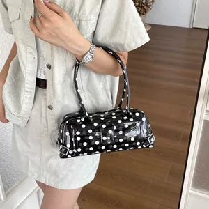 Close-up of a stylish black and white polka dot PVC baguette shoulder bag in use