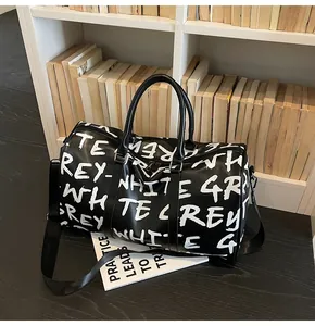 Stylish black travel duffel bag with white graffiti letter print on a shelf background