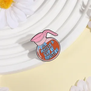 Close-up of pink coffee pot enamel brooch with 'Pour Myself a Cup of Ambition' slogan