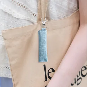 Blue lychee textured leather mini pouch with silver keychain attached to a beige canvas bag