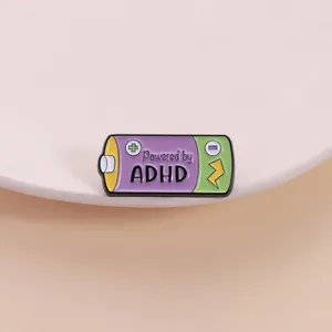 Close-up of a battery enamel pin featuring the text 'Powered by ADHD' in purple and green