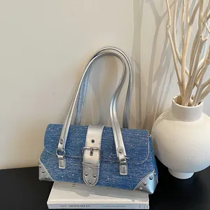 Detail view of denim baguette bag with silver buckle and studs on a book prop