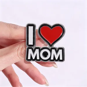 Vista detallada de un pin de esmalte con forma de corazón I Love Mom sostenido por una mano