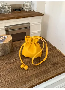Yellow leather drawstring bucket bag with round bead accents on a rustic wooden table