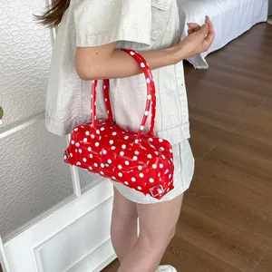 Close-up of a vibrant red and white polka dot PVC baguette shoulder bag on a model