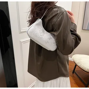 Detail view of a white underarm bag with butterfly patterns on a model's shoulder