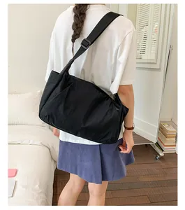 Minimalist black large capacity tote bag worn as a crossbody messenger bag indoors.