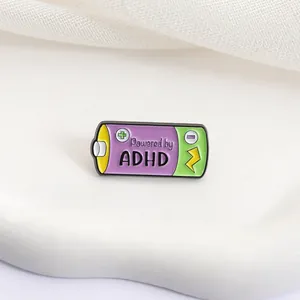 Close-up macro view of a "Powered by ADHD" battery-shaped enamel pin on soft fabric