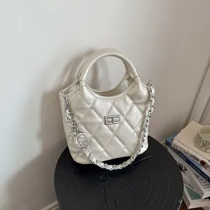 Elegant pearlized beige quilted bucket bag featuring a silver chain strap and unique charm