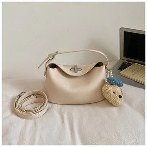Elegant cream bucket handbag featuring a crossbody strap and a cute teddy bear charm