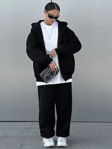 Woman wearing a black oversized zip-up hoodie and sweatpants set in a minimalist setting