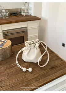 Minimalist cream white drawstring bucket bag on a rustic wooden countertop