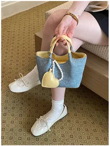Detail view of denim bucket bag with yellow contrast handles and pearl heart charm