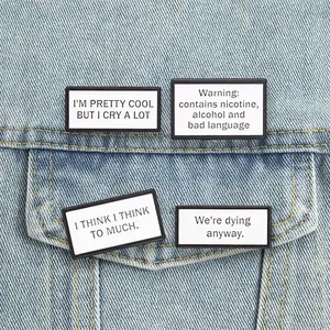 Close-up of rectangular metal pins with funny English slogans on denim jacket pocket