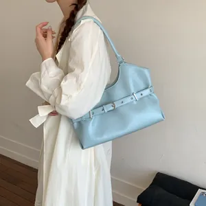 Model wearing a stylish light blue shoulder bag with silver buckle and eyelet detail